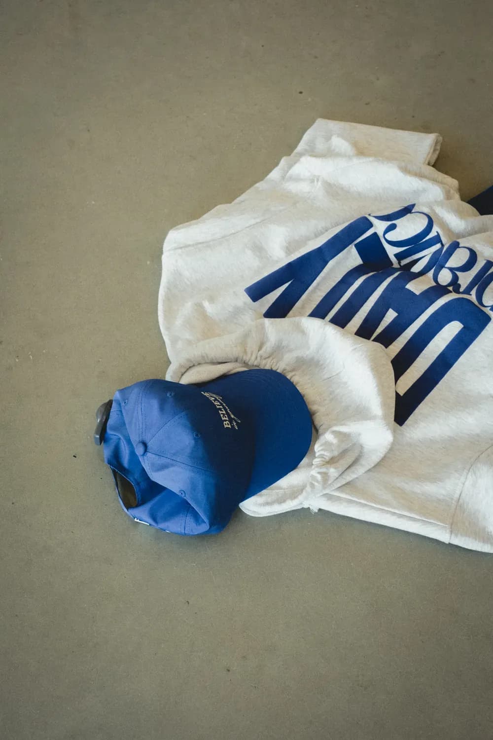 White graphic T-shirt and blue cap laid out on a neutral surface in a casual fashion styling.