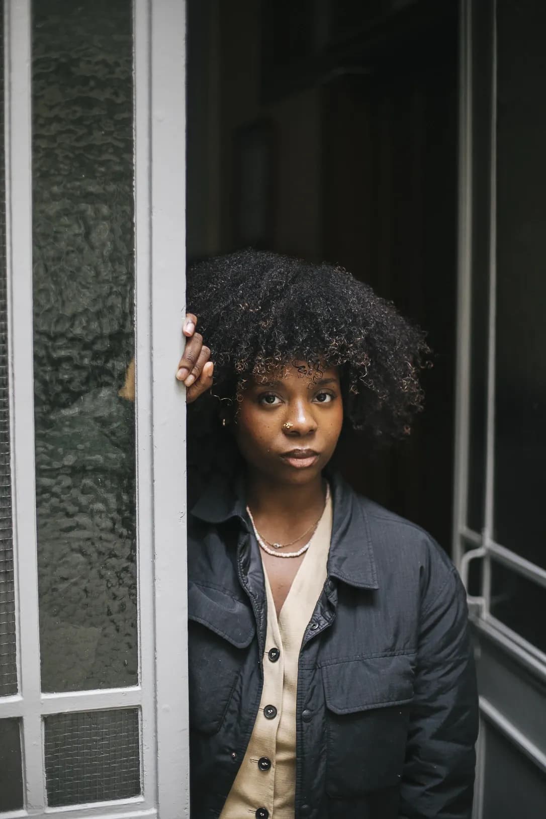 Woman in layered neutral tones standing in a doorway, capturing a subtle and contemporary urban style.