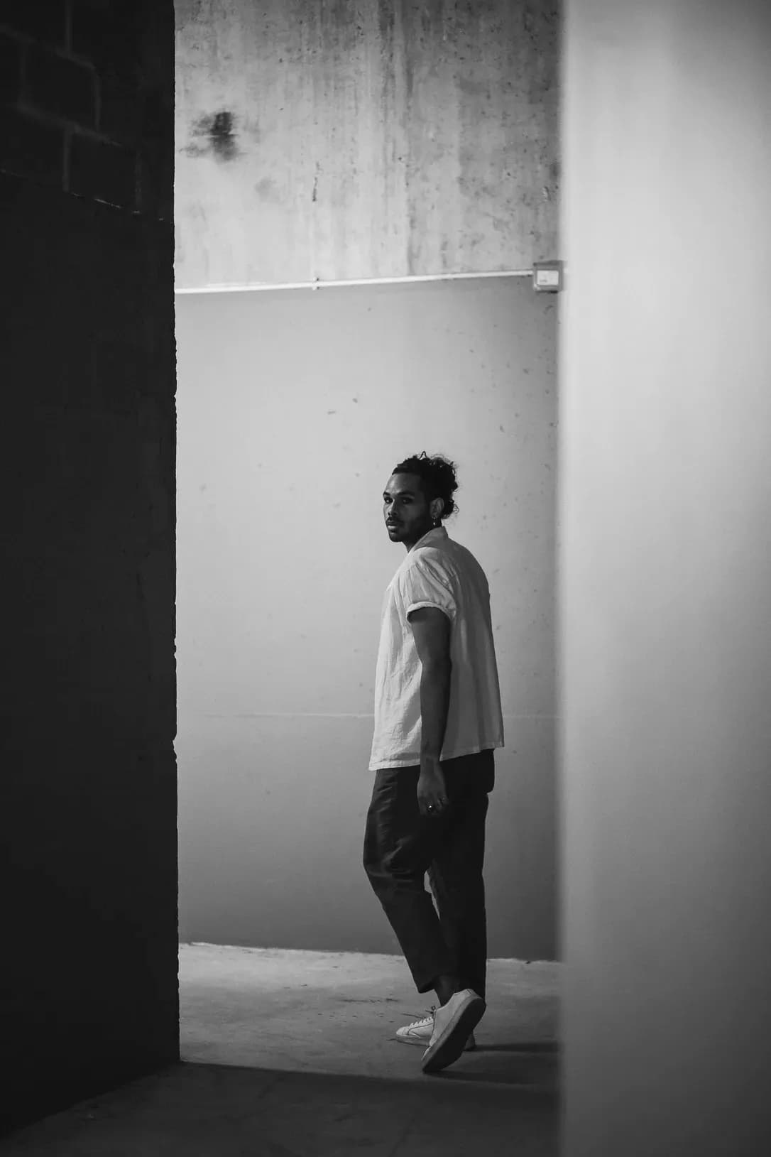 Man in a relaxed tee and trousers walking through a minimalist concrete space, capturing a clean and contemporary style.