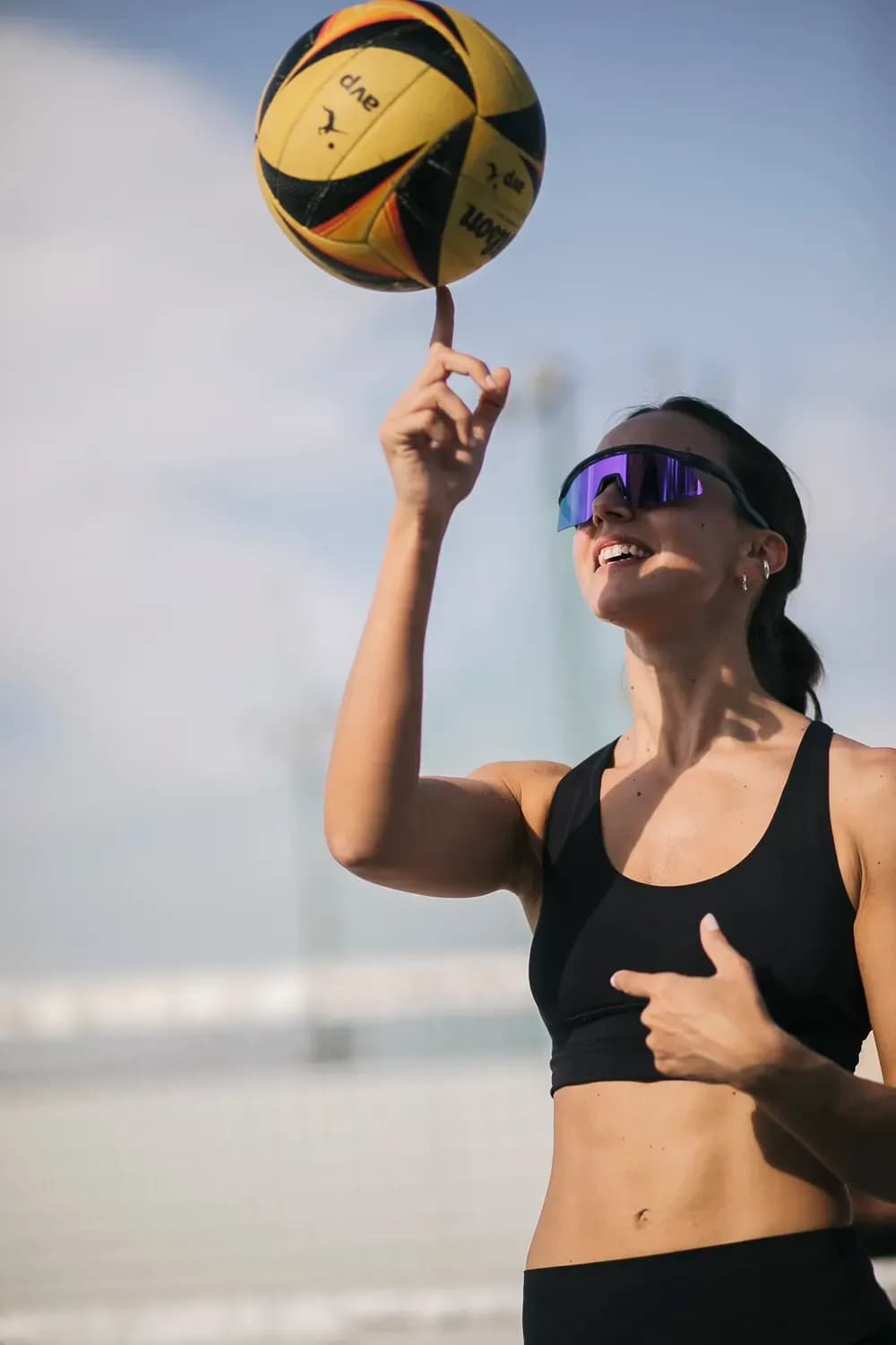 Γυναίκα με αθλητικά μαύρα αθλητικά ρούχα και ανακλαστικά γυαλιά ηλίου που γυρίζει μια μπάλα του μπάσκετ με το δάχτυλό της σε εξωτερικό χώρο κάτω από έναν καθαρό ουρανό.