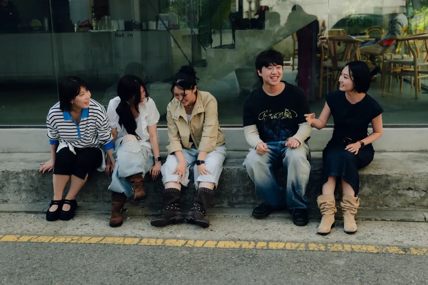 Five friends in contemporary casual clothing sitting together outdoors and enjoying a conversation.