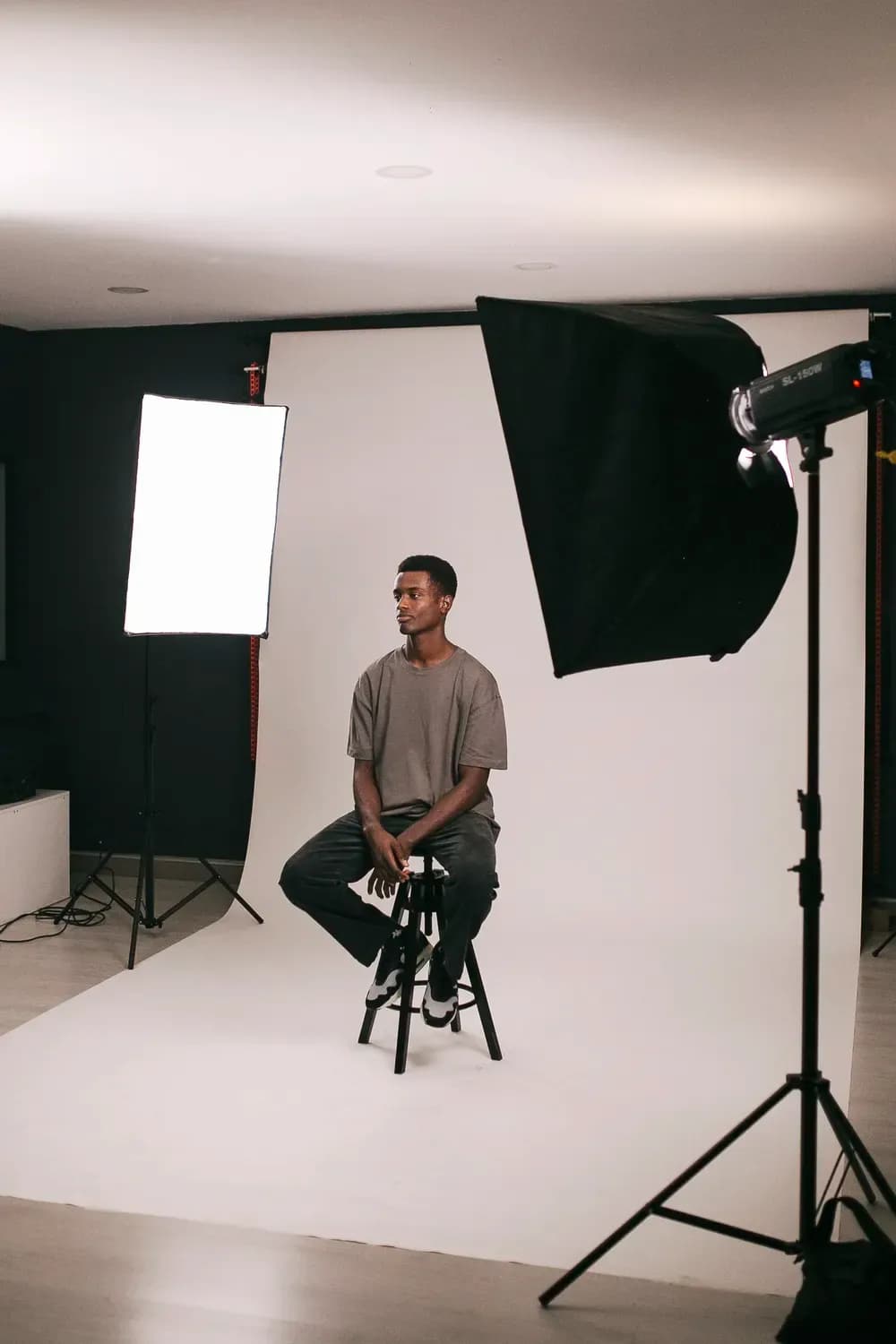 Man sitting on a stool in a photography studio with lighting equipment, captured during a fashion photoshoot setup.