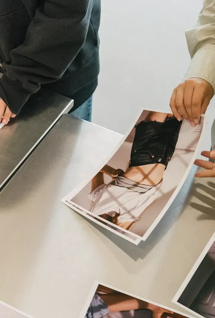 Close-up of hands reviewing printed fashion photographs on a table in a studio setting.