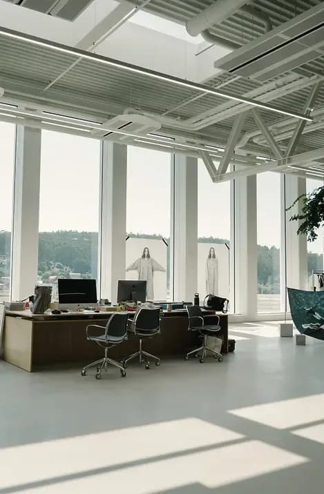 Bright, minimalist fashion studio with large windows, desks and chairs, and garment displays set against a natural landscape backdrop.