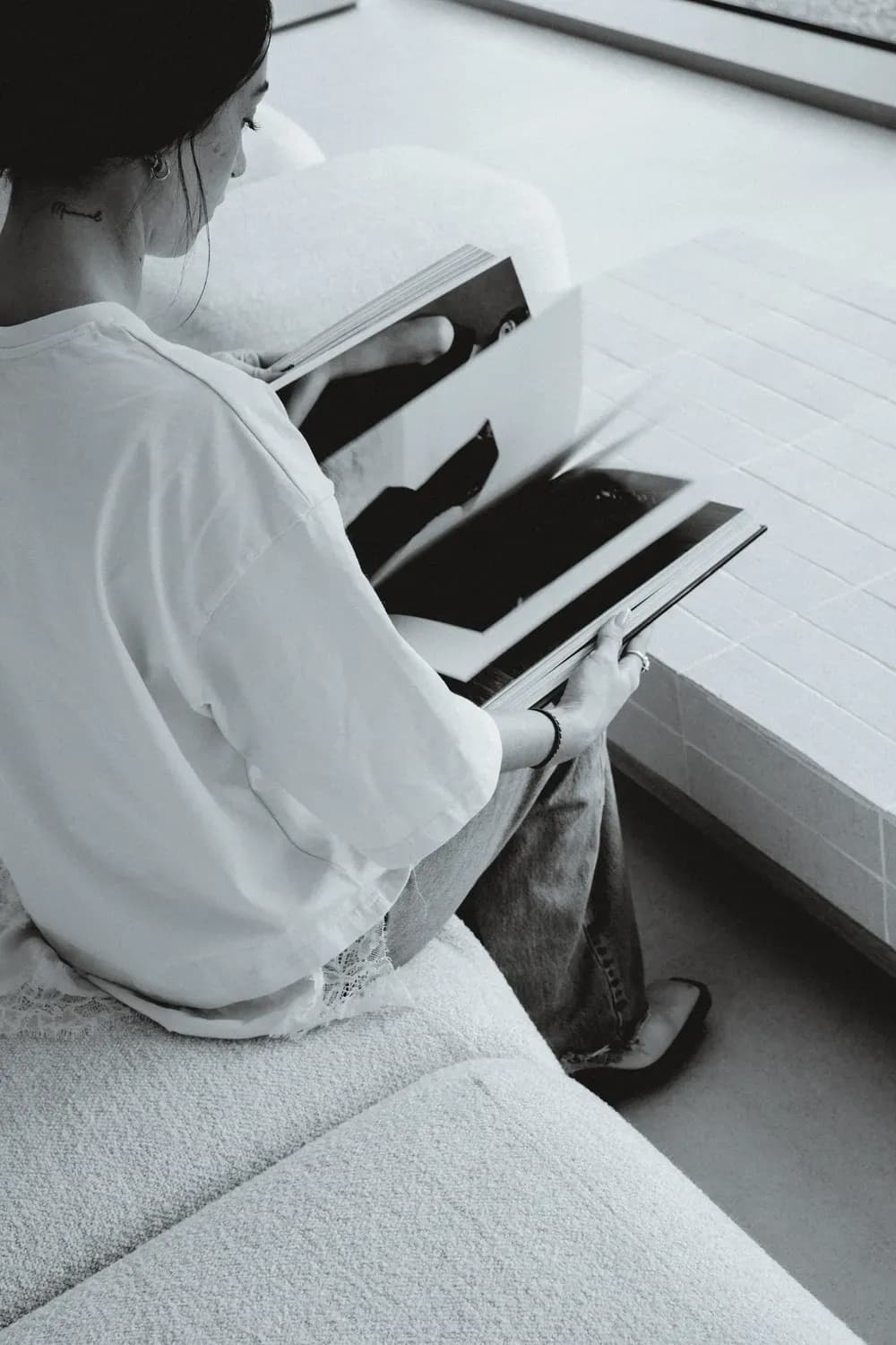 A person sitting by a window, flipping through a large book or magazine in a calm indoor setting.