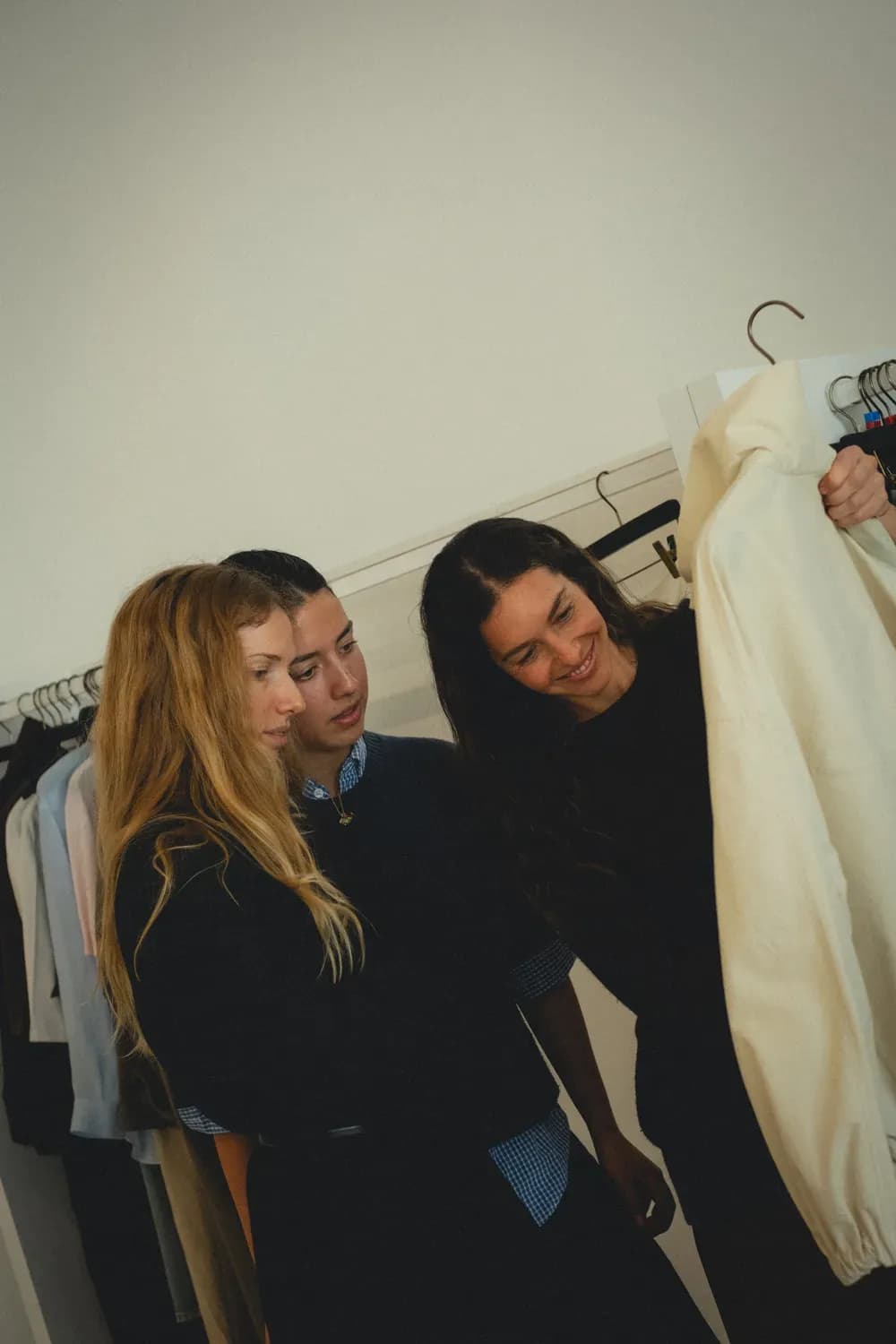Dans un studio, trois personnes examinent un vêtement clair sur un cintre, se concentrant sur son design et son tissu.